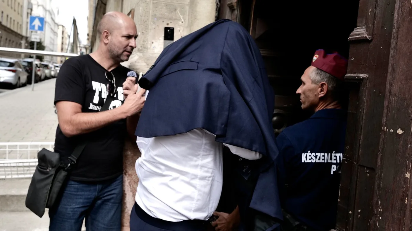 Osumnjičenik prekriven sakoom ulazi u zgradu u pratnji mađarske policije dok mu novinar postavlja pitanja