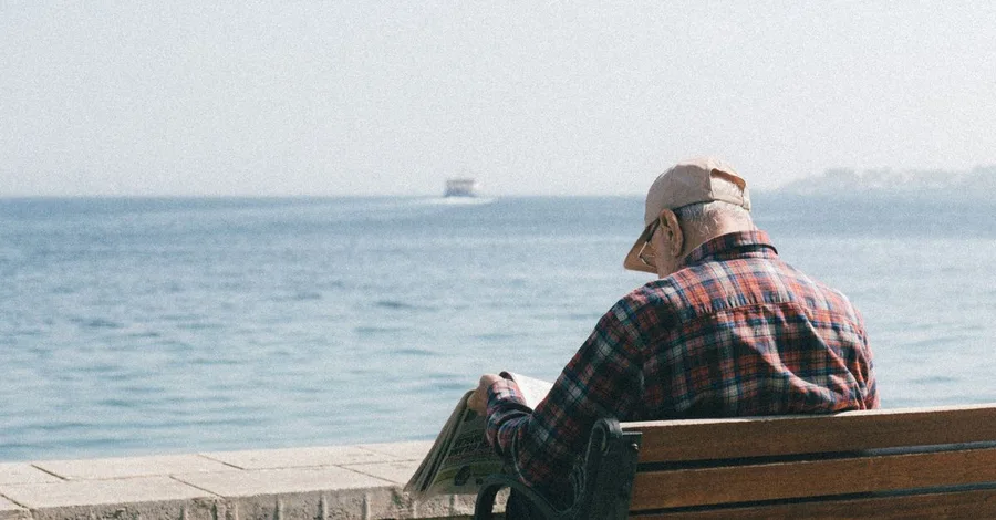 Senior man enjoys reading a newspaper while sitting by the seaside, embracing relaxation.
