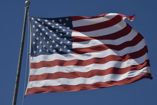 United States flag waving prominently against a clear, bright blue sky, symbolizing patriotism and freedom.